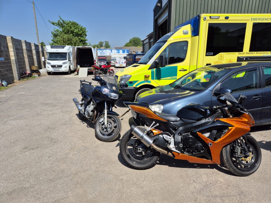 Black and orange motorcycles and a South Western Ambulance parked in a lot under a clear sky.