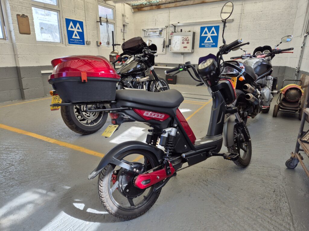A red and gray electric scooter with a storage box parked in a garage with motorcycles.